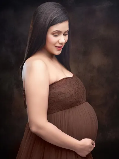 A warm, intimate close-up against a textured brown backdrop. This shot focuses on the gentle expression of the mother-to-be, creating a soft and classic fine-art portrait.