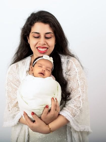 A new mother's joyful smile as she holds her sleeping newborn. The clean, white-on-white styling creates a bright and timeless portrait.