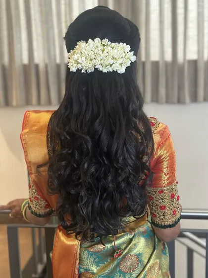 A classic half-updo with soft curls and a fresh jasmine gajra. This hairstyle is a perfect blend of traditional and modern, suitable for any wedding event.
