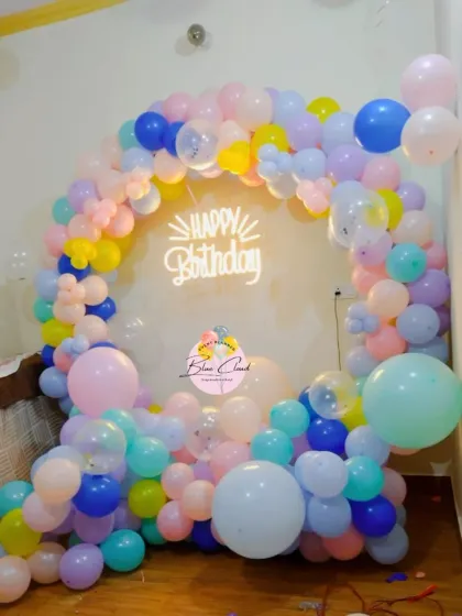 A vibrant pastel rainbow balloon ring with a 'Happy Birthday' neon sign.