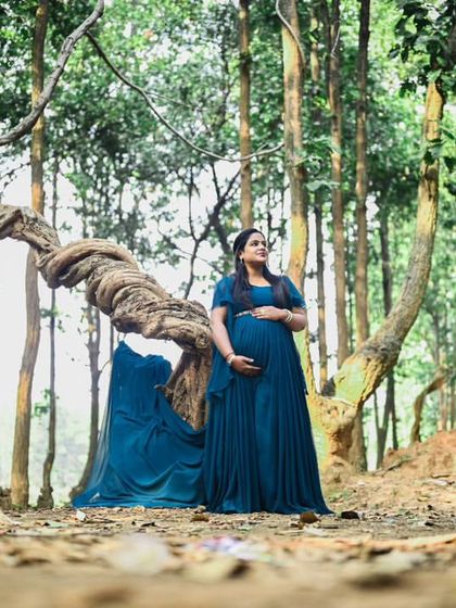 A stunning wide-angle shot of an expectant mother in a flowing blue gown, standing by a unique, twisted tree in the forest. This creates a powerful and ethereal maternity portrait.