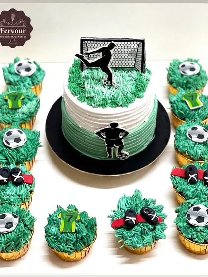 A football theme cake that comes with matching cupcakes. The main cake is a Lotus Biscoff flavour, and the set is decorated with grass-like frosting and football-themed toppers.