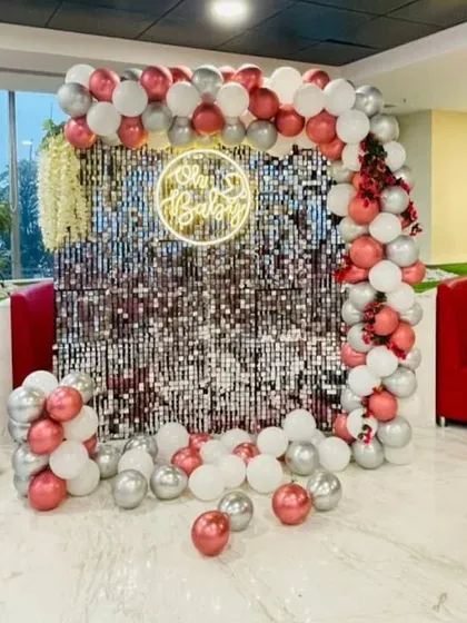 A chic party backdrop with a silver shimmer wall and a balloon arch in chrome pink, silver, and white.
