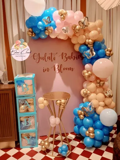 A 'Gulati Babies in Bloom' baby shower with a custom backdrop, 'BABY' blocks, and a blue, peach, and gold balloon garland.