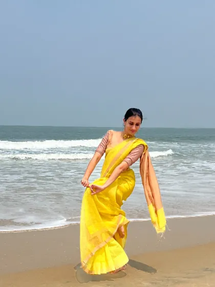 A classic dance pose in a vibrant yellow saree on the beach. This is an example of a dance-inspired modeling pose, where the posture and lines of the body complement the flow of the garment.