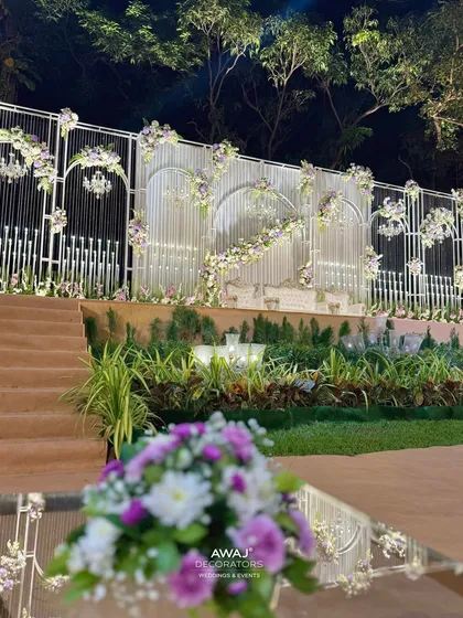 A detailed shot of the stage, focusing on the intricate white framework, hanging crystal elements, and the beautiful blend of white and purple flowers.