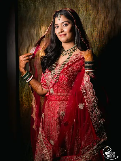 A stunning portrait of a bride in a rich red lehenga, holding her veil.