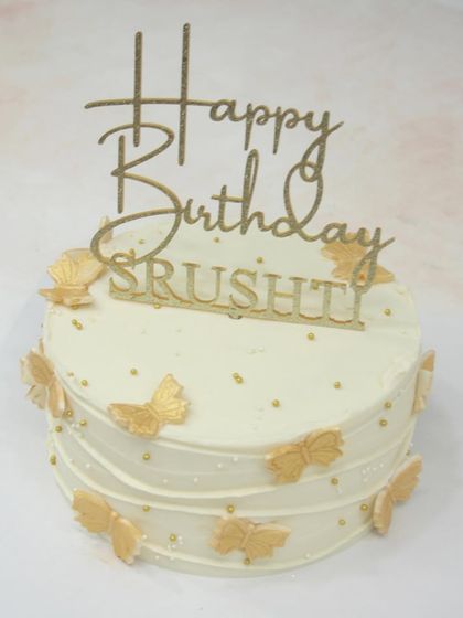 A stunning all-white cake adorned with handmade golden butterflies and a personalized name topper. The simplicity of the design makes it incredibly elegant.