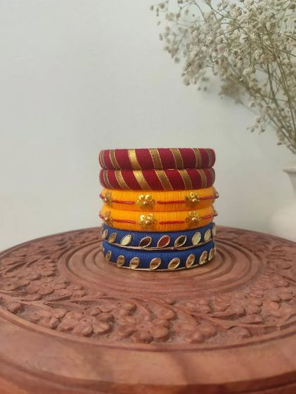 This stack of thread bangles in red, yellow, and blue is a classic festive combination. The set includes different designs, from gota patti work to mirror embellishments.