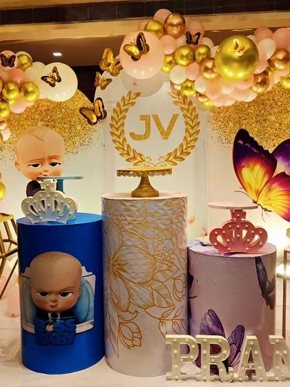 A glamorous joint celebration featuring Boss Baby and Butterfly themes. The decor includes gold and pink balloons, character cutouts, and a custom 'JV' monogram.