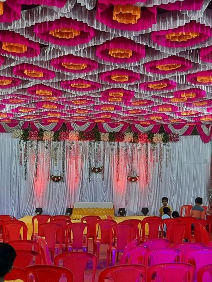 A wide view of the seating arrangement inside a beautifully decorated pandal for a Haldi event, with a vibrant pink, yellow, and white ceiling.