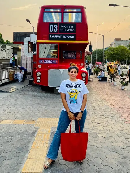 A casual summer look with a Minions graphic tee and flared jeans, posing in front of a cool red double-decker food bus in Delhi.