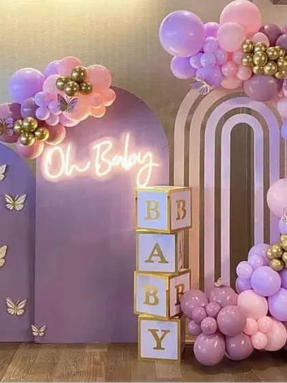 This pastel baby shower decoration is one of my most requested styles. It features custom-built lavender arched panels with delicate butterfly accents, an "Oh Baby" neon sign, and a stunning organic balloon garland in shades of lilac, pink, and gold. The stacked "BABY" blocks complete this elegant and modern photo-ready backdrop.