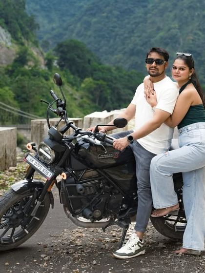 A stylish pose with the motorcycle on a mountain road. This photo captures the cool, adventurous vibe of the couple and their Rishikesh pre-wedding shoot.