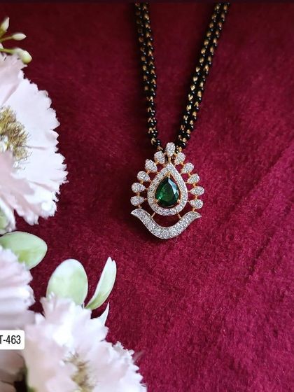 This mangalsutra features a beautiful pendant with a central green stone surrounded by American diamonds. It's a classic design with a touch of color.