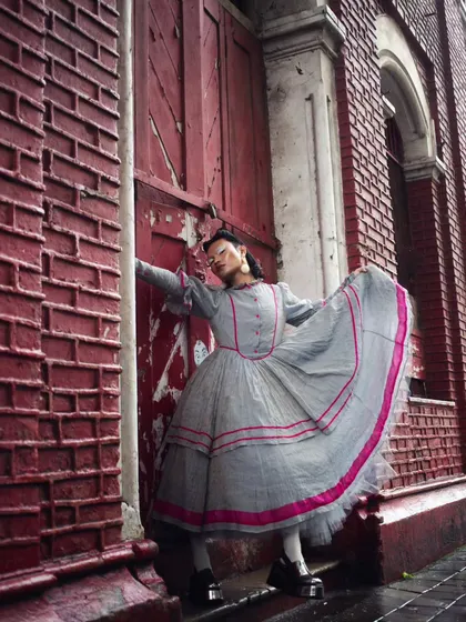 The architecture of the city becomes a backdrop for rebellion. The model's period-inspired dress with modern twists stands out against the textured brick wall, a key shot from the "RIOT" editorial.