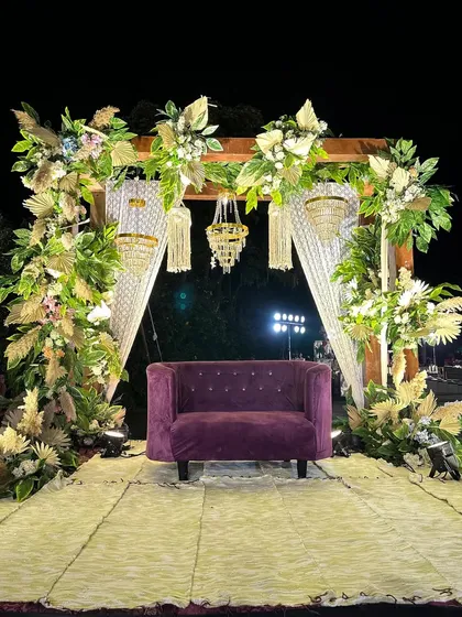 A chic and rustic seating area for the bride and groom, featuring a purple sofa, pampas grass, and elegant chandeliers.