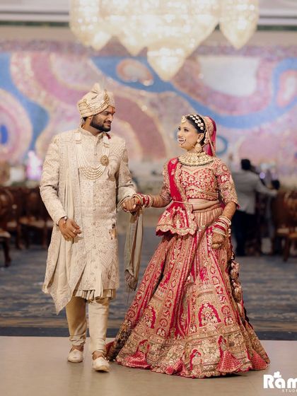 A classic walking shot of the newly married couple, hand in hand, looking at each other with love. The grandeur of the venue is visible in the background.