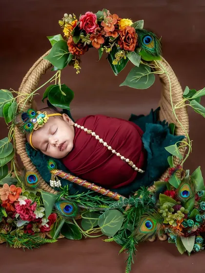 Another beautiful angle of our little Krishna, swaddled in rich maroon fabric and adorned with a pearl necklace and peacock feather headband.