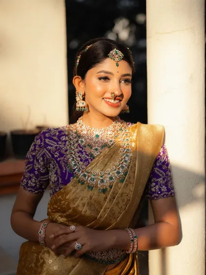 A portrait of actress Rachana Inder in a stunning golden and purple saree. The sunlight catches the intricate details of the jewelry and the rich fabric, creating a radiant look.