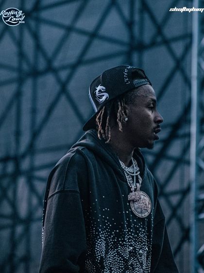 A candid side-profile of Rich the Kid backstage or on the side of the stage at Rolling Loud India. This shot offers a more relaxed, behind-the-scenes feel.