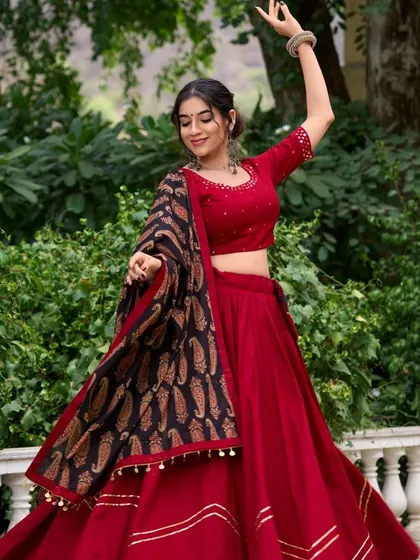 A classic red chaniya choli with a black paisley print dupatta. This timeless look is always in style for Navratri. The model's dance pose shows how beautifully the outfit moves.