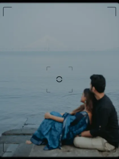 An atmospheric shot of the couple by the sea, with the Bandra-Worli Sea Link faintly visible, framed like a vintage film still.
