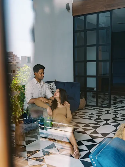 A quiet moment captured through a reflection. This artistic shot shows the couple sitting together on the floor, a glimpse into their life before the baby arrives, full of peaceful anticipation.