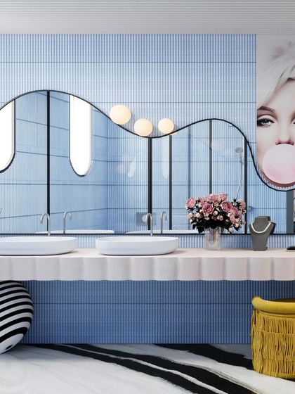 The double vanity is a statement piece, with a long, wavy mirror and quirky yellow stools adding a pop of color.