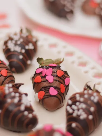 A close-up of a single chocolate-covered strawberry, adorned with pink and red hearts. Each one is hand-dipped and decorated to be a perfect bite of love.