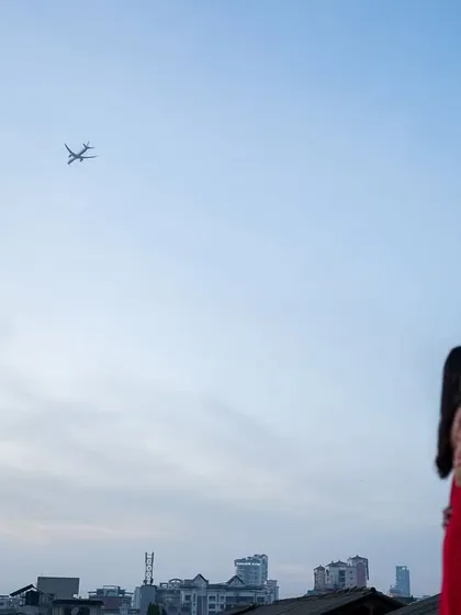 A wide, cinematic frame capturing the couple against the city skyline, with a plane flying overhead. This shot adds a layer of storytelling, suggesting travel, destiny, and a love story in a modern world.