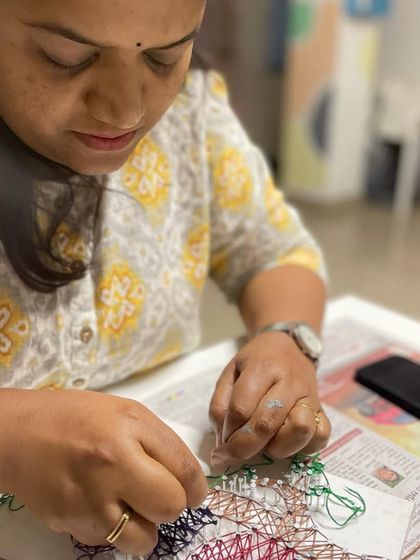 A participant is fully engaged in the therapeutic process of weaving threads for her string art project.
