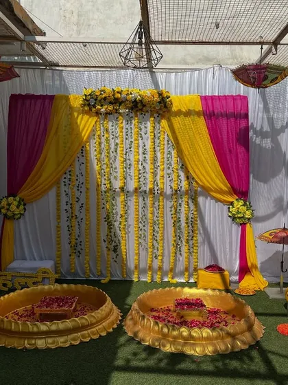 An outdoor haldi setup with a white, yellow, and pink theme. The decor includes two lotus bowls for the ceremony and Rajasthani umbrellas.
