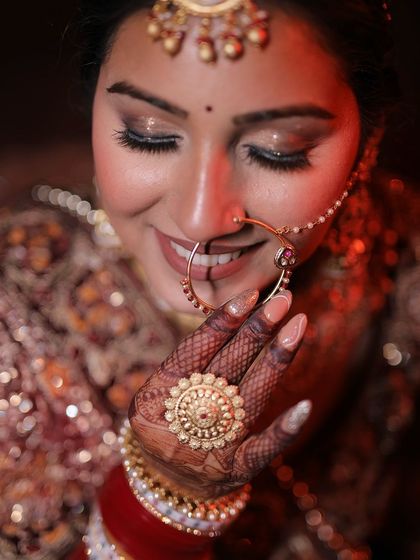 A close-up of a bride's face, focusing on her smile and the large ring on her mehendi-covered hand.