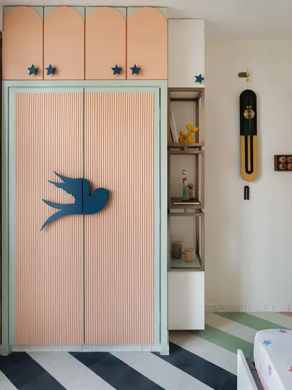 The wardrobe in the kids' room features a fluted pattern in pastel pink and green, with charming bird-shaped and star-shaped handles, adding to the room's whimsical and cozy ambiance.