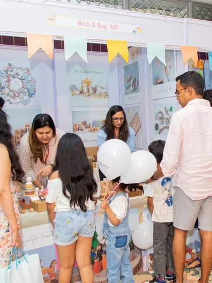 A busy stall with families and kids exploring the products. The white balloons add to the festive, celebratory feel of the shopping experience.