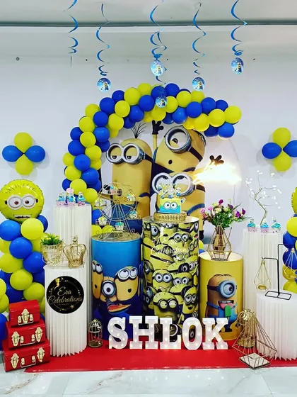 A complete Minions-themed setup for a first birthday. It features character-printed plinths, a number '1' balloon, and fun spiral decorations hanging from the ceiling.