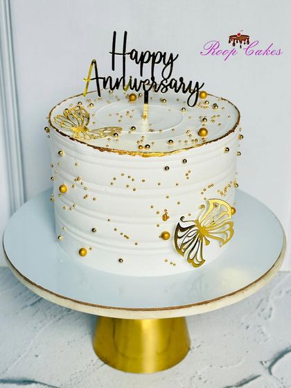 A simple yet beautiful anniversary cake in white and gold, adorned with delicate butterflies.