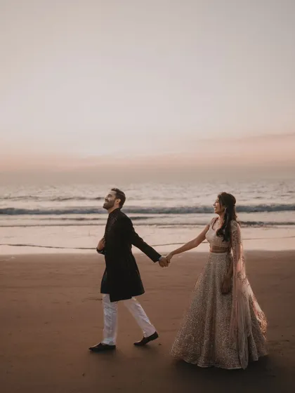 A candid moment of the couple walking hand-in-hand on the beach, the perfect quiet moment during a lively Sangeet celebration.