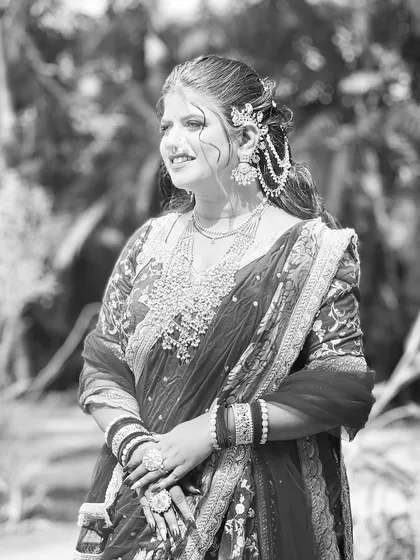 A beautiful black and white photo of a bride in an outdoor setting. Her hairstyle, featuring an elegant updo with accessories, looks timeless.