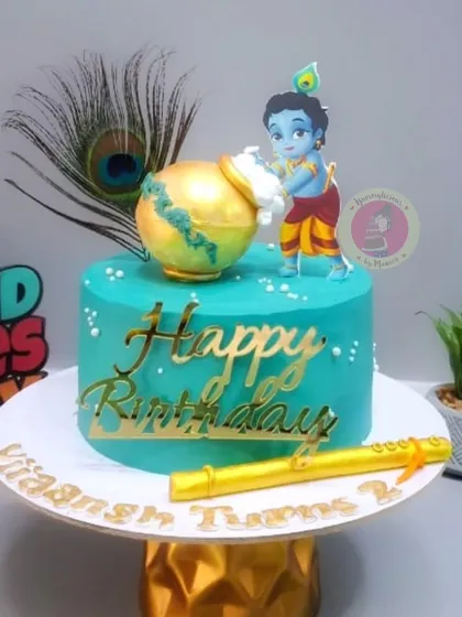 A beautiful Krishna-themed birthday cake with a golden matki and a flute.