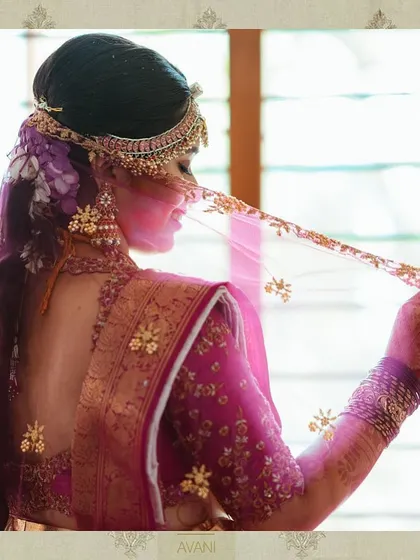 A bride in a deep pink saree with a matching embroidered blouse. The sheer, embroidered veil adds a touch of ethereal beauty to her look.