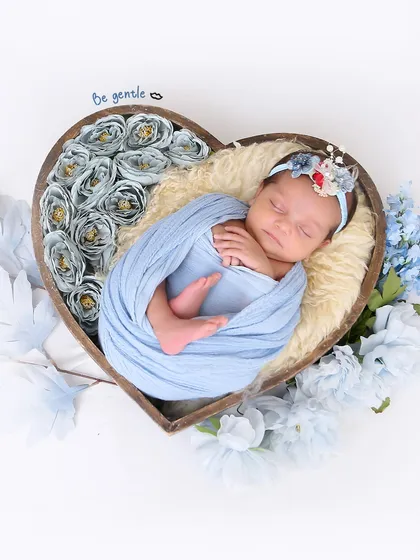 A newborn rests peacefully in a heart-shaped bowl filled with soft blue flowers. This is an example of a creative and artistic setup for a newborn photoshoot.