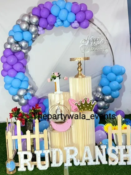A cool-toned ring decoration with purple, blue, and silver balloons. The setup is placed on an artificial grass mat, which adds a nice touch of color.