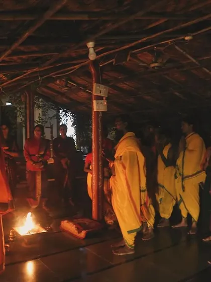 Students stand in prayer during a nighttime ceremony. The flickering flames of the havan create an atmosphere of deep reverence and connection to the divine.