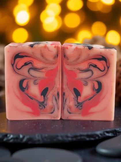 A beautiful butterfly swirl soap with a dramatic red, pink, and black design. The bokeh background makes the colors pop, highlighting the artistry in the pour.