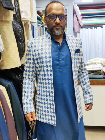 A client wearing a blue and white diamond-patterned open shrug over a solid blue Pathani suit. This is a great example of how to layer patterns and solids for a show-stopping look.