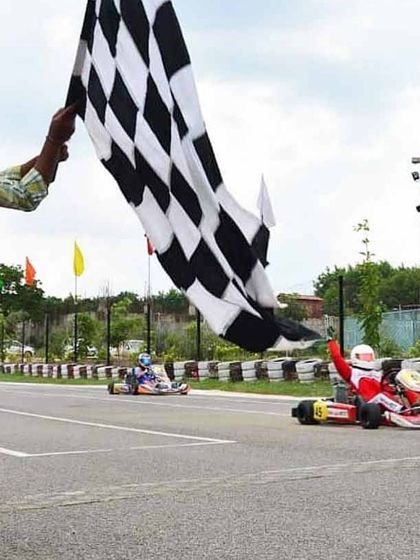 A driver in our Birel ART kart crosses the finish line with a hand raised in victory, capturing the exhilarating moment of winning a race.