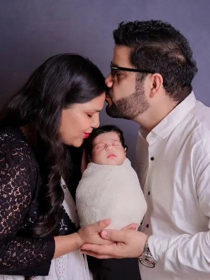 A full-body portrait of a new family, with the father holding the baby and the mother looking on lovingly. This is a timeless pose that showcases the family unit.