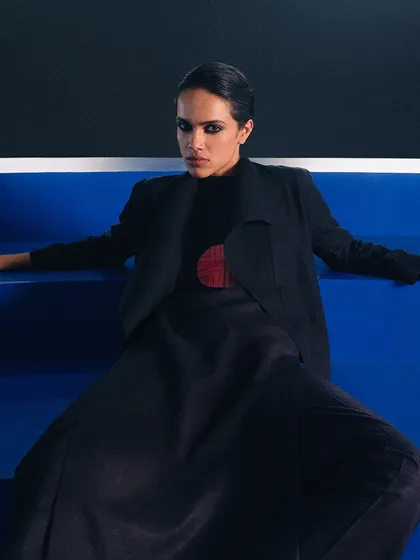 A closer shot of the model seated on the blue steps. The styling is sharp and tailored, with a pop of red that echoes the architectural details in other shots.